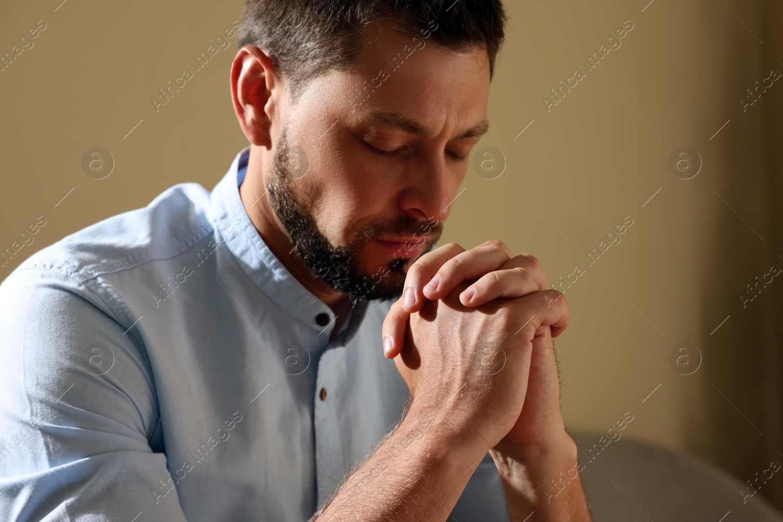 Photo of Religious man with clasped hands praying indoors