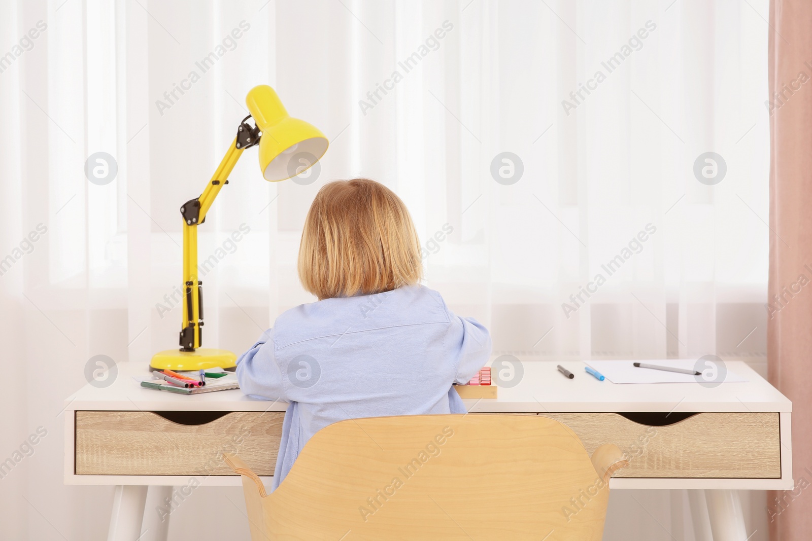 Photo of Little boy sitting at desk in room, back view. Home workplace