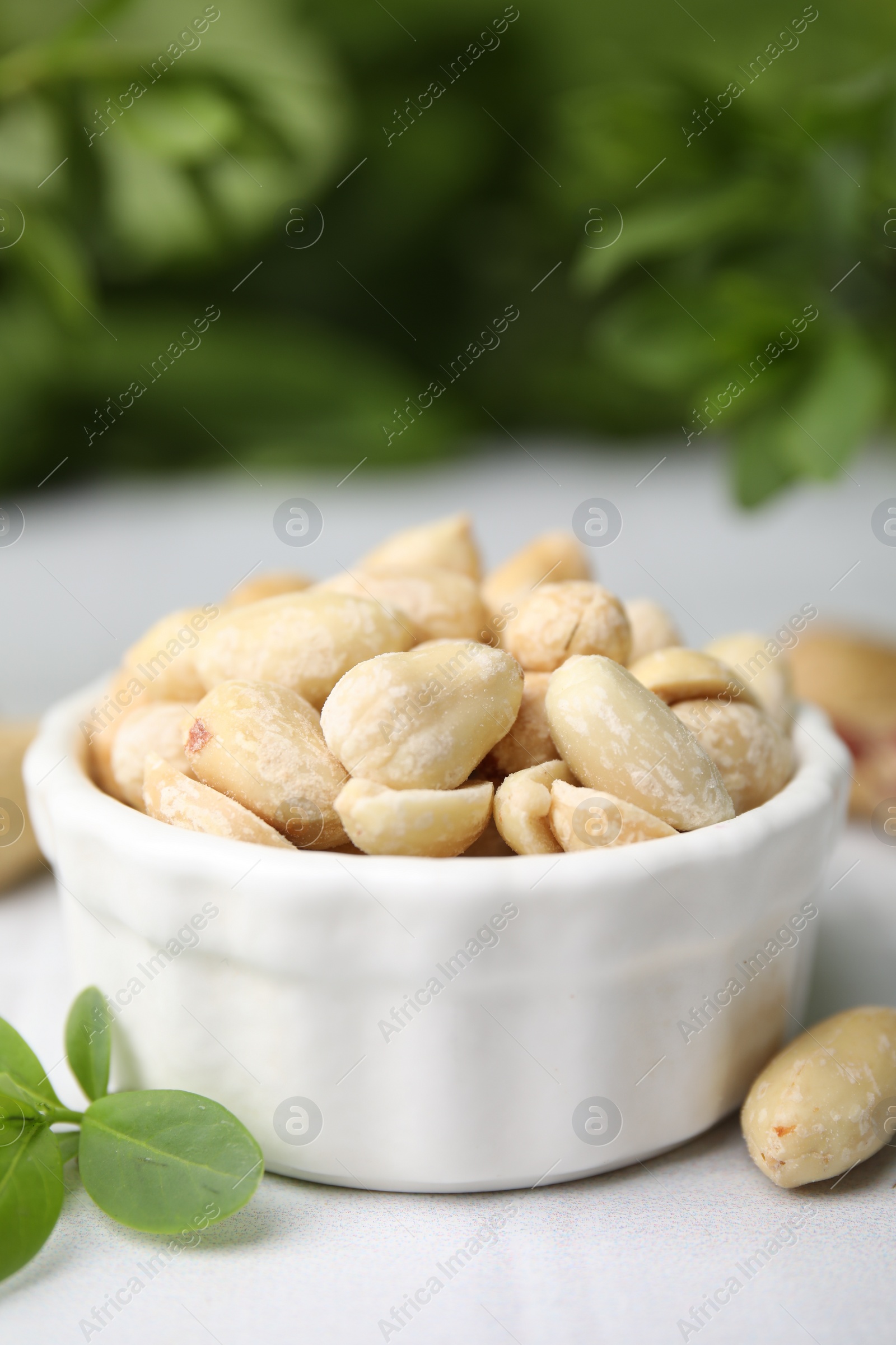 Photo of Fresh peeled peanuts in bowl on white tiled table against blurred green background, closeup