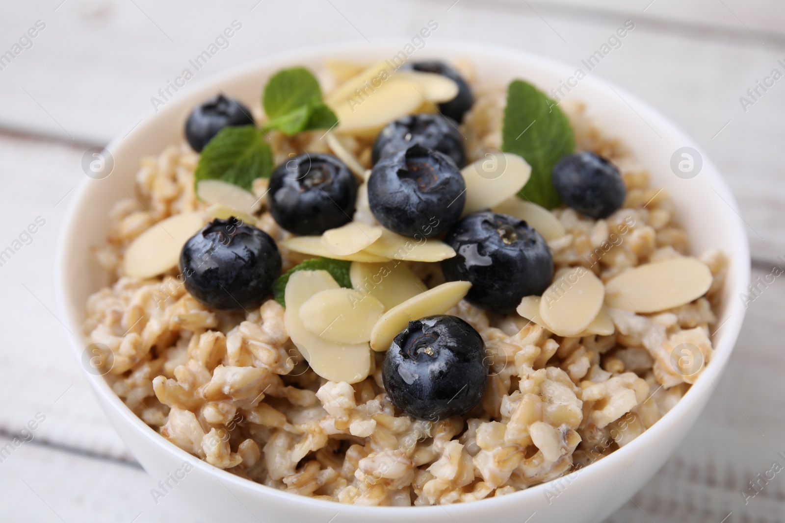 Photo of Tasty oatmeal with blueberries, mint and almond petals in bowl on wooden table, closeup