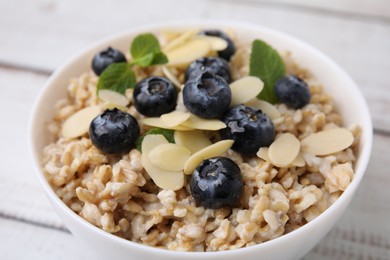 Photo of Tasty oatmeal with blueberries, mint and almond petals in bowl on wooden table, closeup