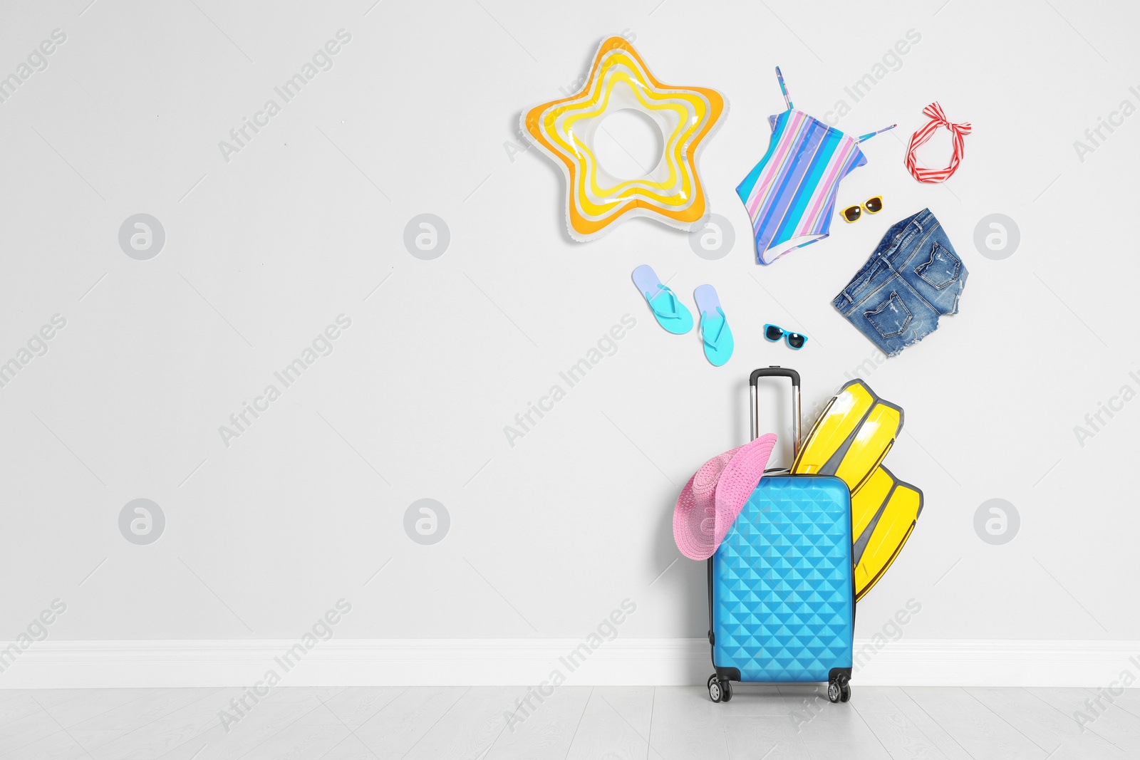 Photo of Composition with suitcase and beach accessories near light wall. Space for text