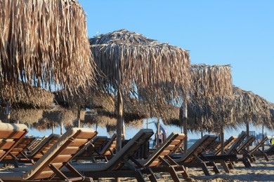 Photo of Beautiful straw umbrellas and wooden sunbeds on beach