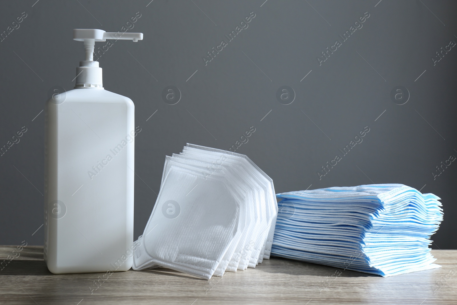 Photo of Hand sanitizer and respiratory masks on wooden table against grey background. Protective essentials during COVID-19 pandemic