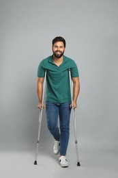 Photo of Young man with axillary crutches on grey background