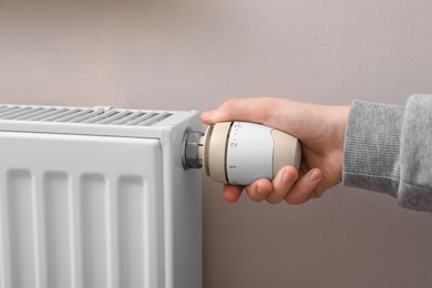 Photo of Girl adjusting heating radiator thermostat near white wall, closeup