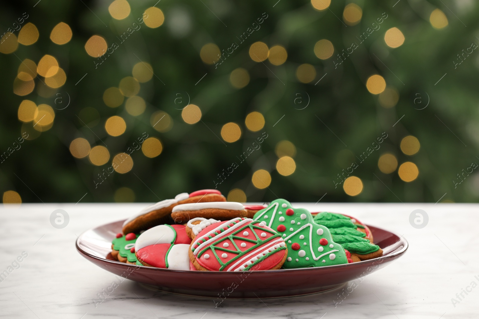 Photo of Decorated cookies on white marble table against blurred Christmas lights