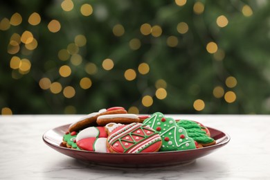 Decorated cookies on white marble table against blurred Christmas lights