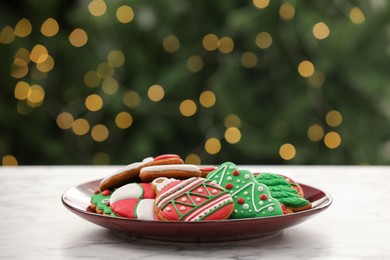 Photo of Decorated cookies on white marble table against blurred Christmas lights