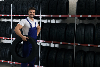Male mechanic with car tire in auto store