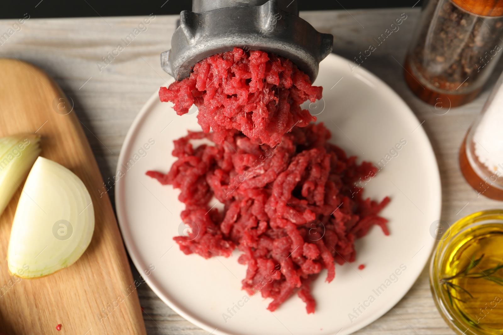 Photo of Mincing beef with metal meat grinder on light wooden table, closeup