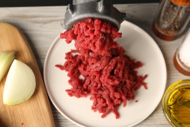 Mincing beef with metal meat grinder on light wooden table, closeup