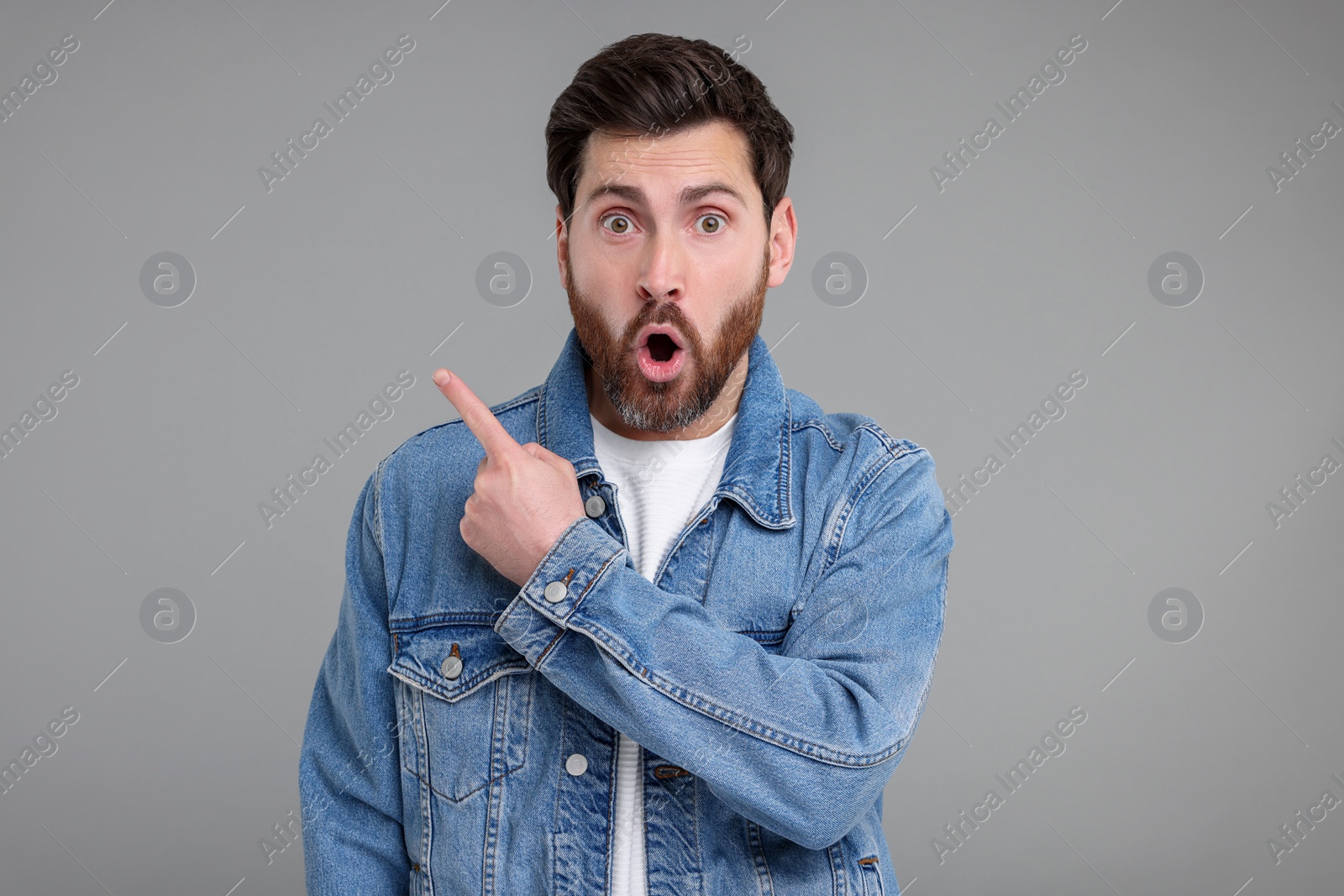 Photo of Surprised man pointing at something on grey background