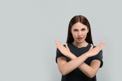 Photo of Stop gesture. Woman with crossed hands on grey background, space for text