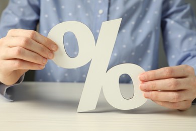 Woman holding percent sign at white wooden table, closeup