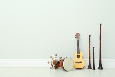 Ukulele, vintage bryolkas, tambourine and hand drum near white wall indoors, space for text. Musical instruments