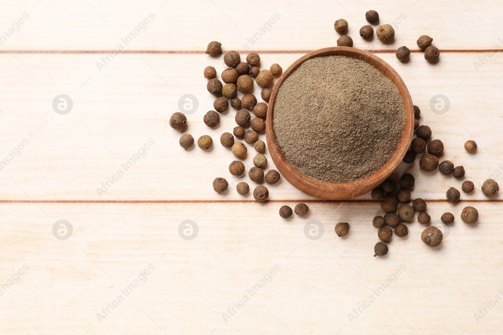 Photo of Ground and whole allspice berries (Jamaica pepper) in bowl on light wooden table, top view. Space for text