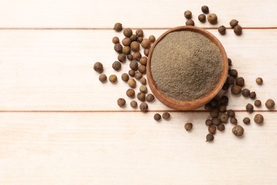 Ground and whole allspice berries (Jamaica pepper) in bowl on light wooden table, top view. Space for text