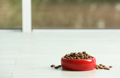 Photo of Bowl with dry dog food on white floor indoors, space for text