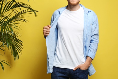 Young man wearing blank t-shirt on yellow background, closeup. Mockup for design