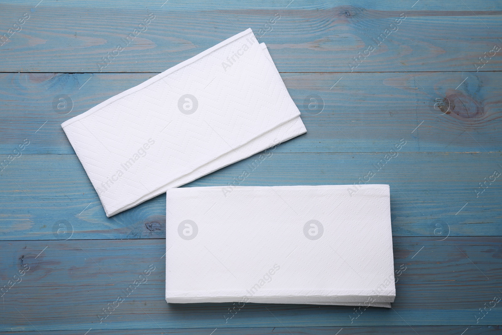 Photo of Clean tissue towels on light blue wooden table, flat lay