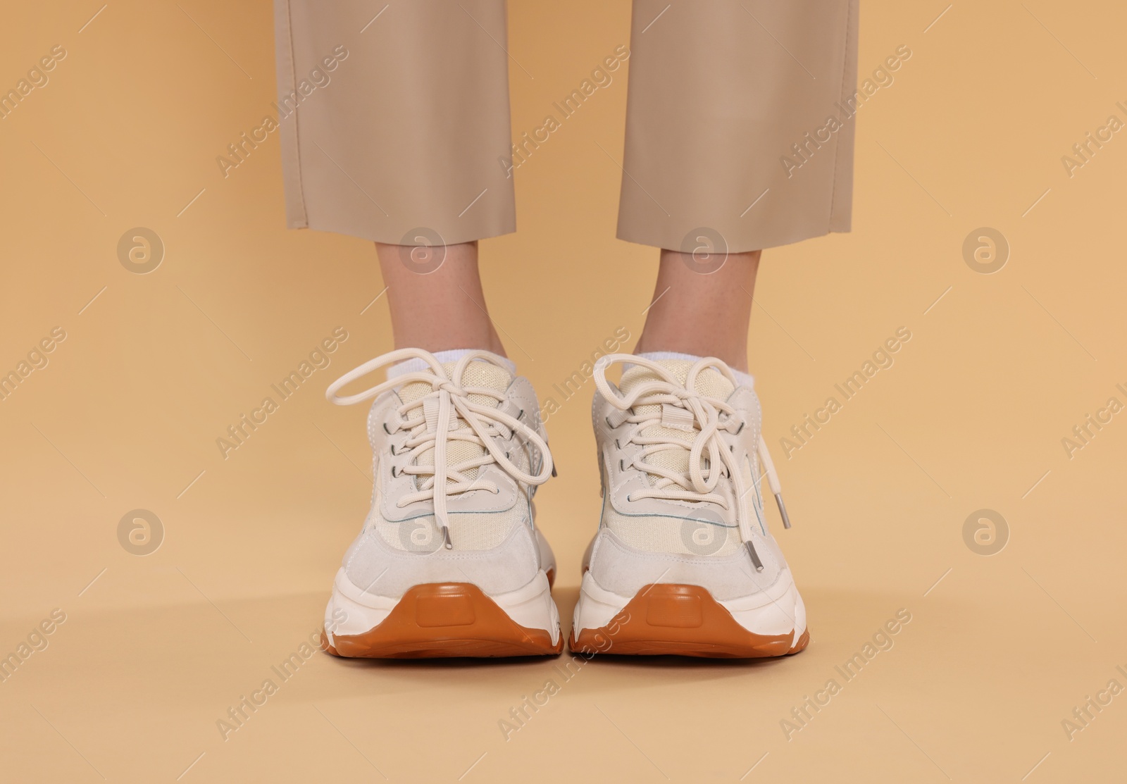 Photo of Woman wearing pair of new stylish sneakers on beige background, closeup