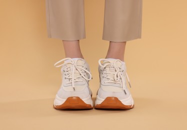 Woman wearing pair of new stylish sneakers on beige background, closeup