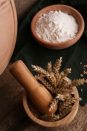 Photo of Mortar with spikes and bowl of wheat flour on wooden table