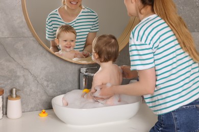 Mother washing her little baby in sink at home