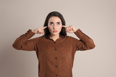 Young woman covering ears with fingers on beige background