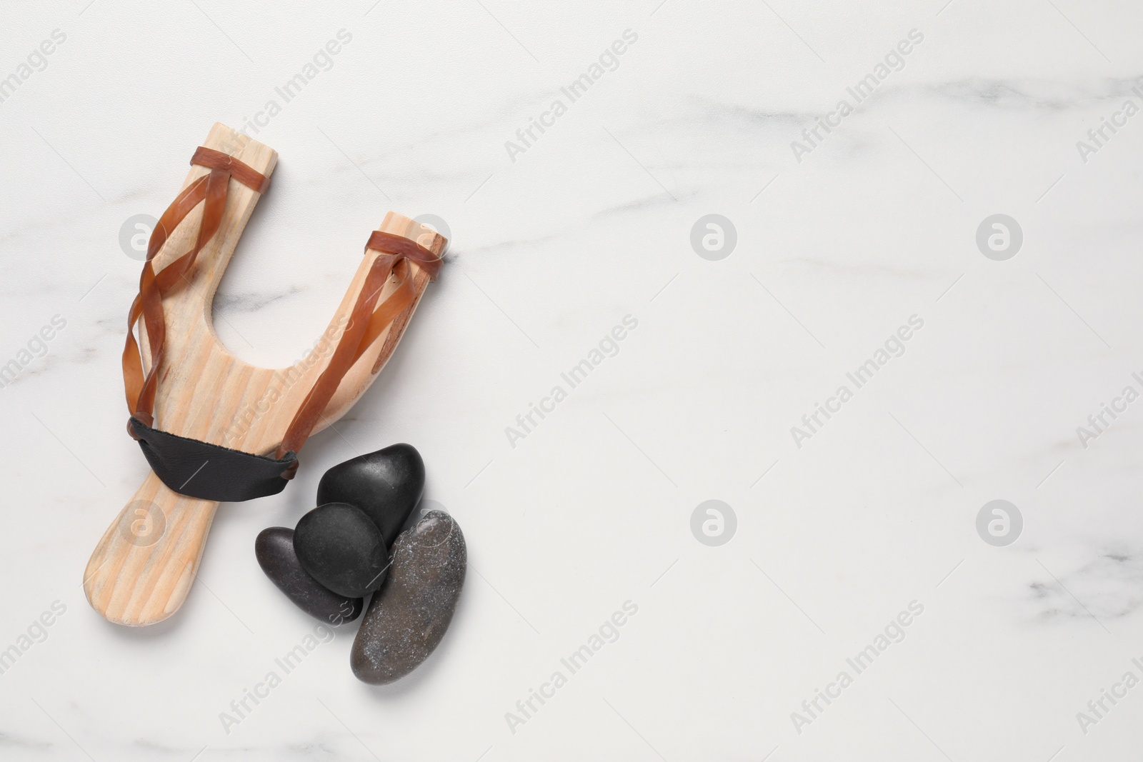 Photo of Wooden slingshot with stones on white marble background, flat lay. Space for text