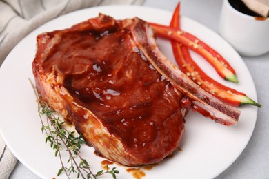 Photo of Raw marinated meat with thyme and chili pepper on light table, closeup