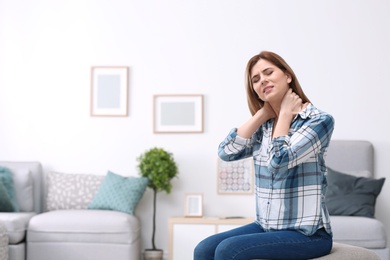 Photo of Young woman suffering from neck pain at home