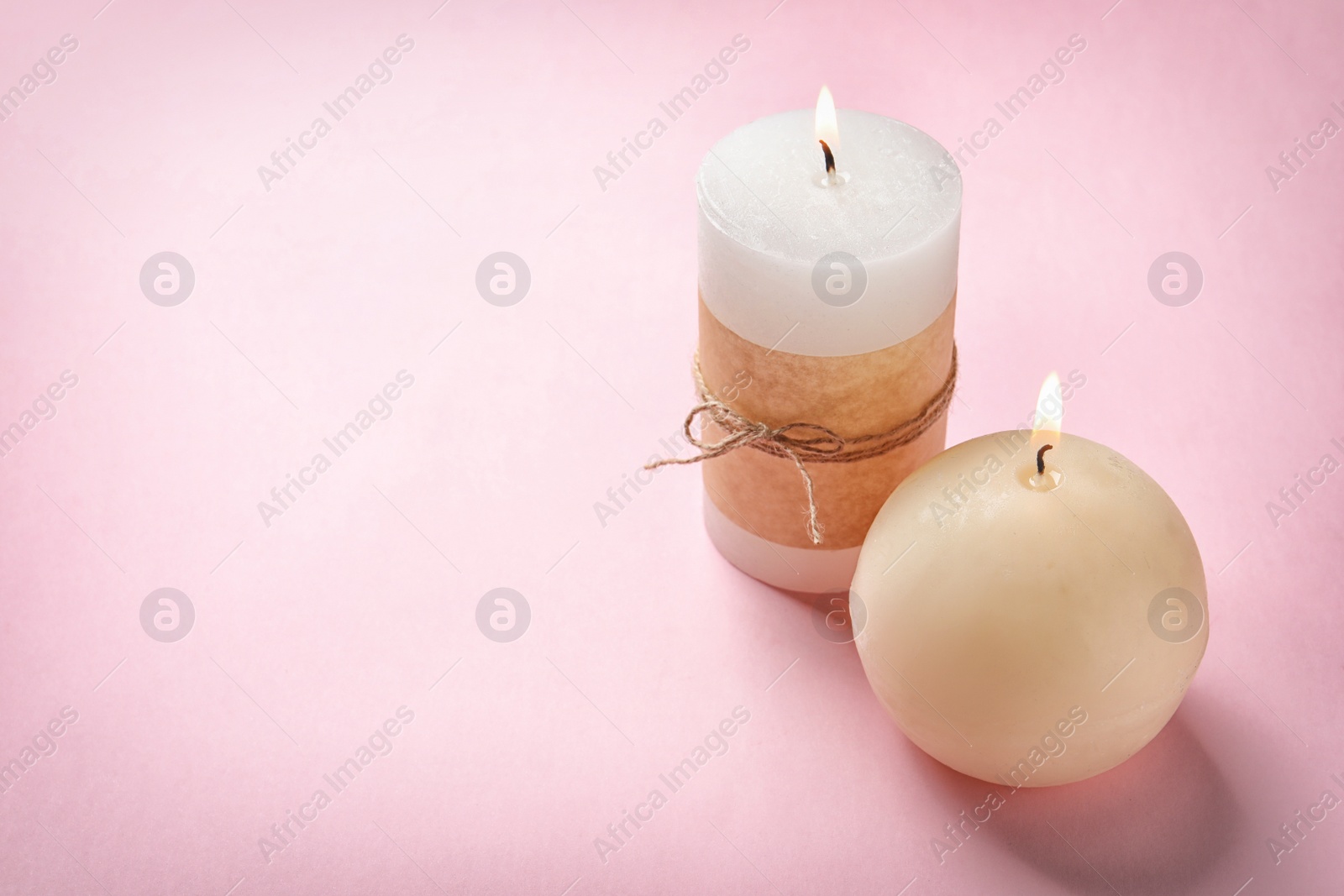 Photo of Burning wax candles of different shapes on color background