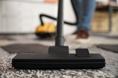 Young man cleaning carpet with vacuum cleaner at home, closeup