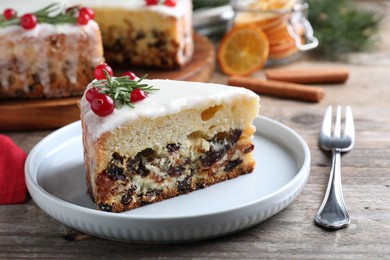Slice of traditional Christmas cake decorated with rosemary and cranberries on wooden table, closeup