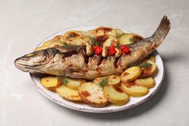 Photo of Plate with delicious baked sea bass fish and potatoes on light table