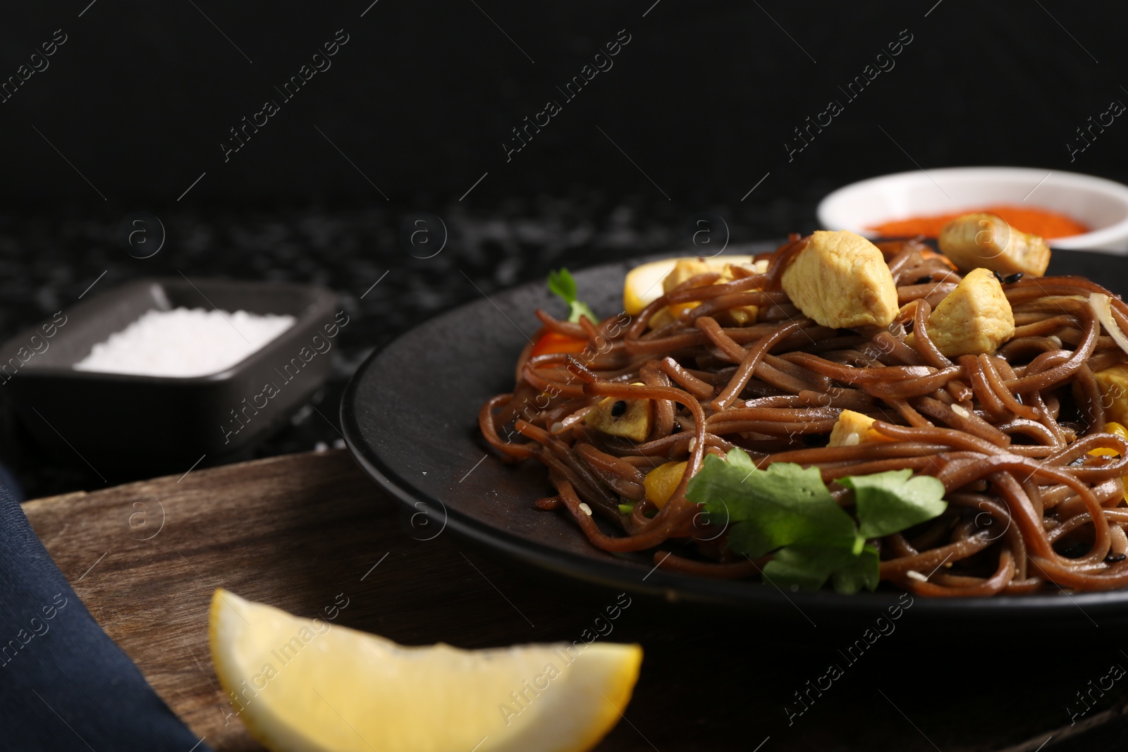 Photo of Stir-fry. Tasty noodles with vegetables and meat on dark table, closeup