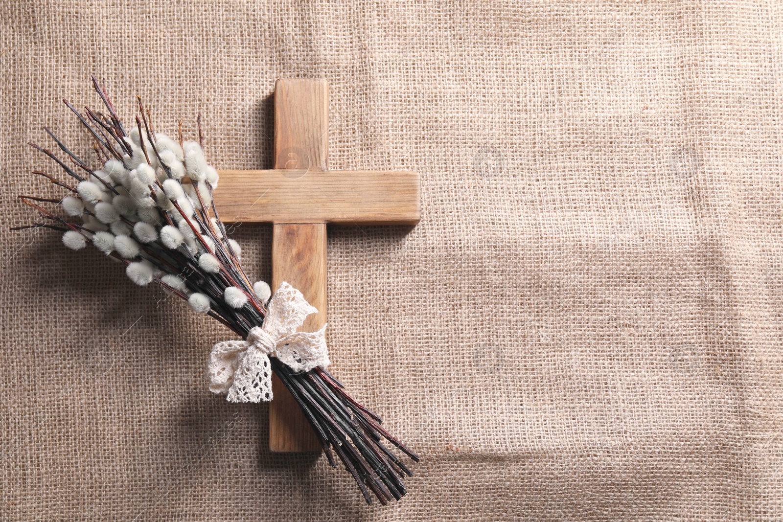 Photo of Cross and willow branches on beige cloth, flat lay. Space for text