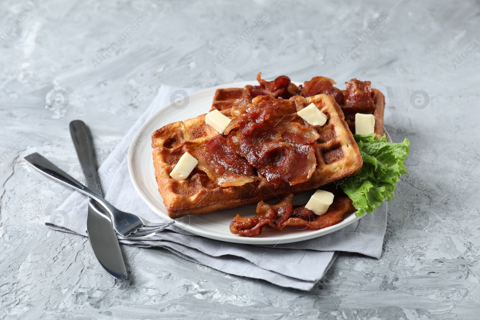 Photo of Delicious Belgium waffles served with fried bacon and butter on grey table