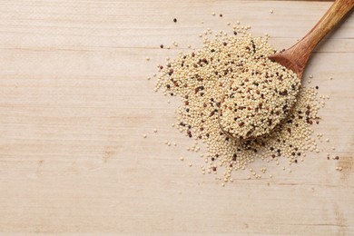Photo of Spoon with raw quinoa seeds on wooden table, top view. Space for text