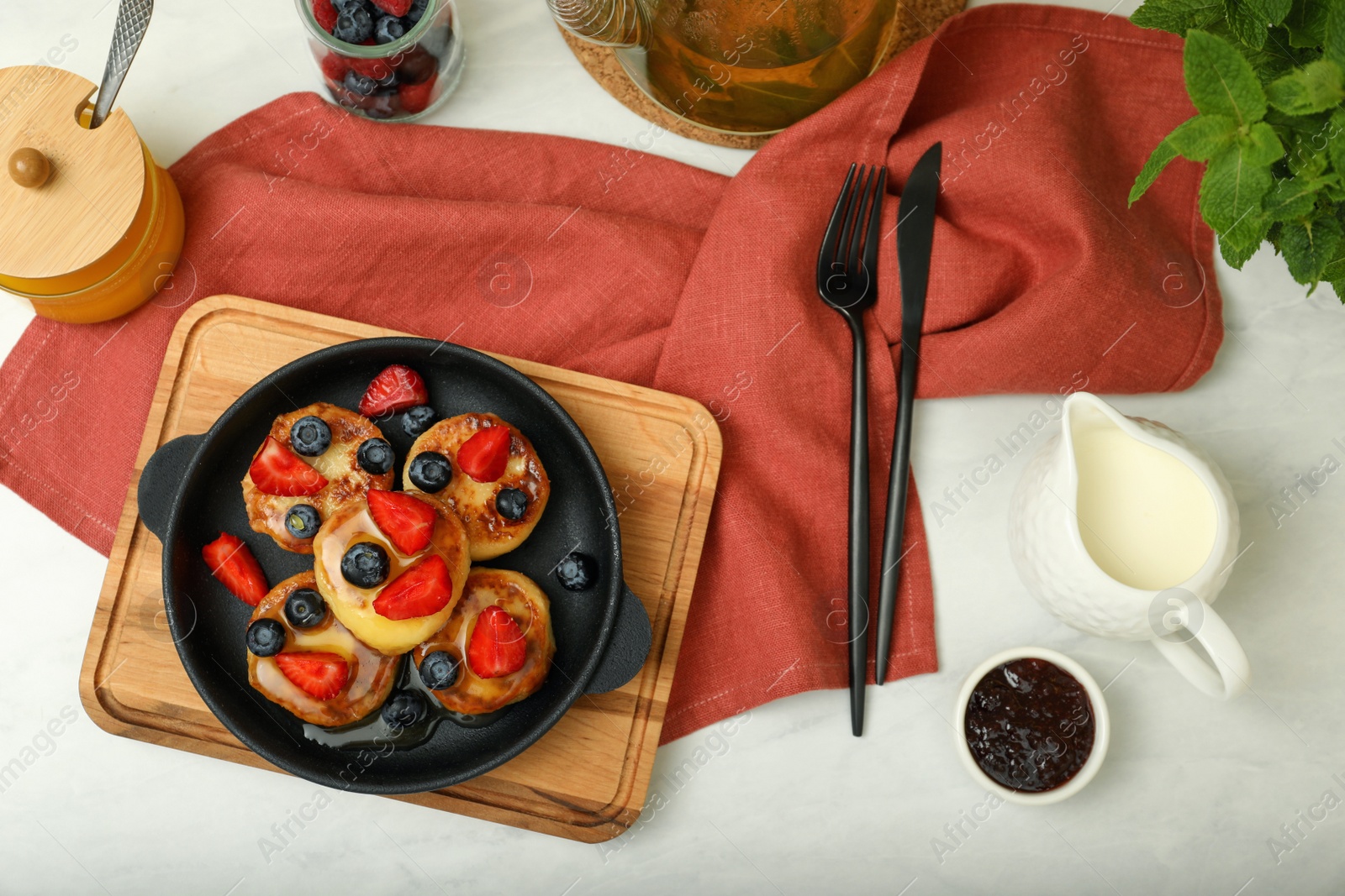 Photo of Delicious cottage cheese pancakes with fresh berries and honey served on white table, flat lay