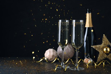 Photo of Happy New Year! Bottle of sparkling wine, glasses and festive decor on black background, space for text