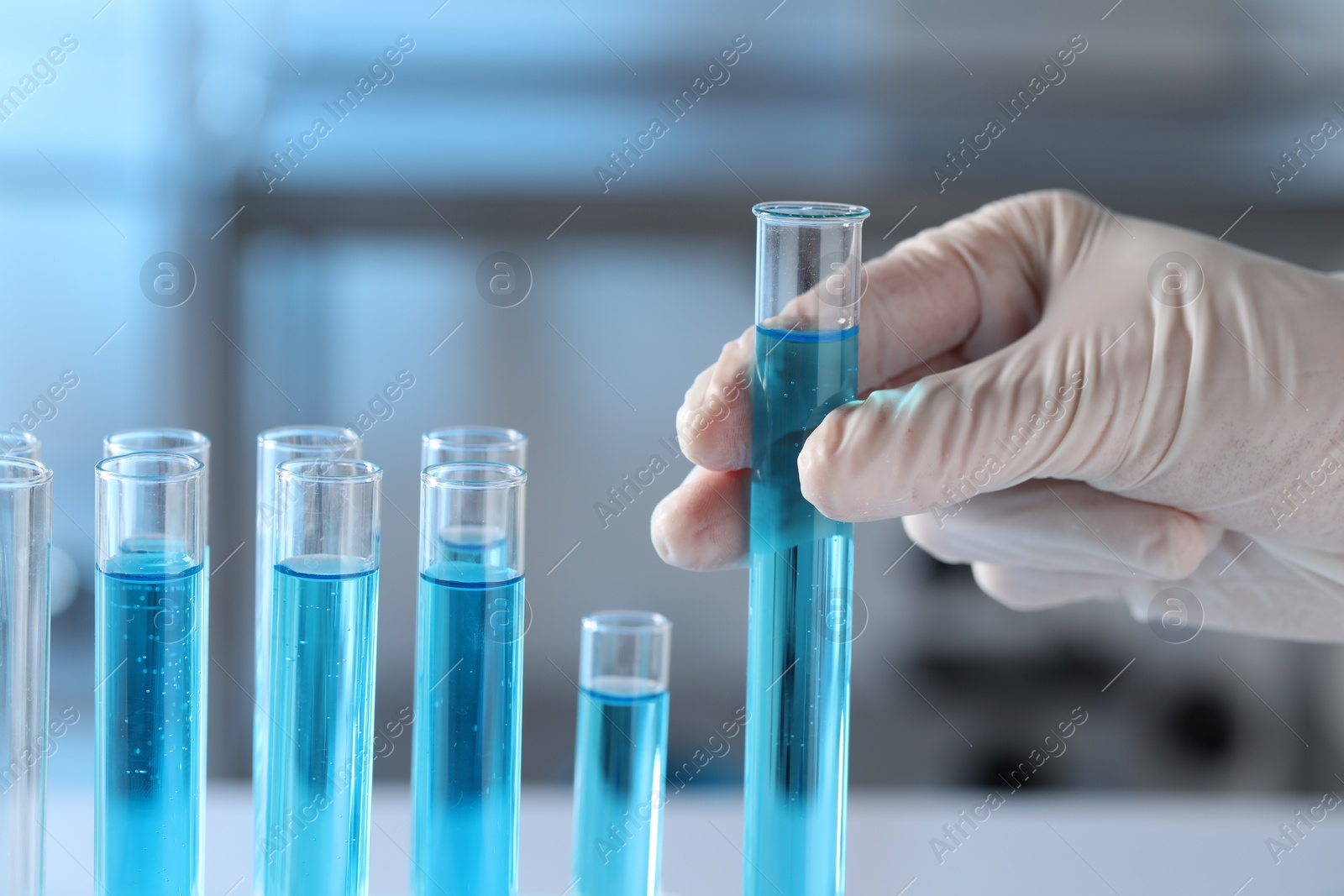 Photo of Scientist taking test tube with light blue liquid in laboratory, closeup