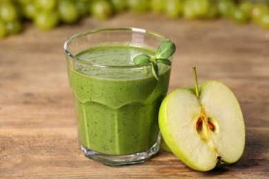 Photo of Glass of fresh green smoothie and cut apple on wooden table