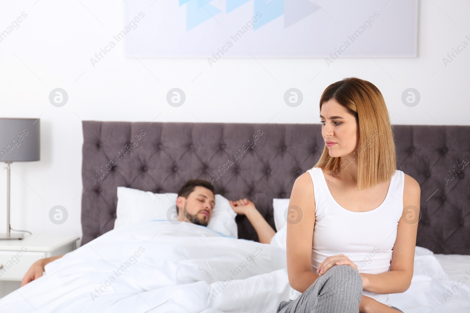 Photo of Upset woman sitting on bed near her sleeping husband at home. Relationship problems
