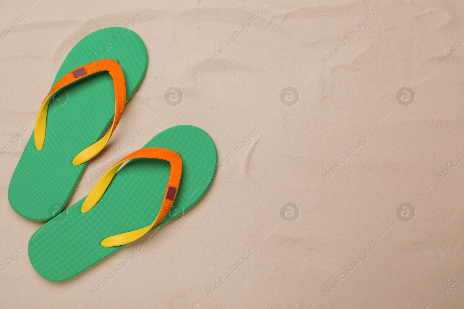 Photo of Pair of green flip flops on sand, flat lay. Space for text