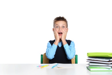 Emotional little boy in uniform with school stationery at desk against white background