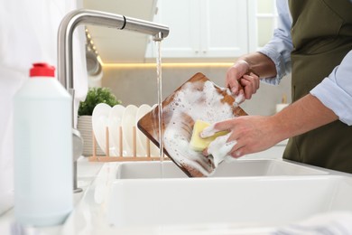 Photo of Man washing wooden cutting board in kitchen sink, closeup