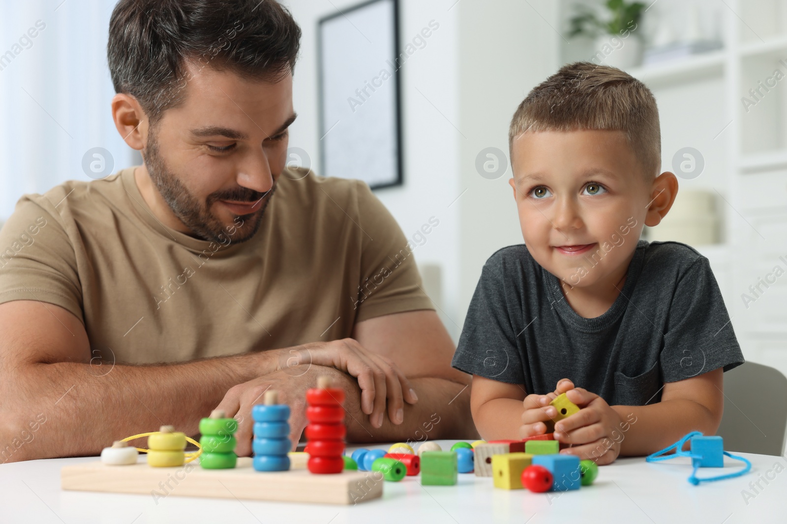 Photo of Motor skills development. Father and his son playing with stacking and counting game at table indoors